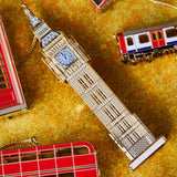 Exquisite handcrafted Big Ben Christmas ornament by The London Christmas Company, featuring intricate 24K gold detailing, displayed alongside iconic London double-decker bus and subway tube train ornaments. Perfect for adding British charm to holiday decor.