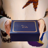 Woman's hands holding luxury blue gift box with gold details and The London Christmas Company logo.