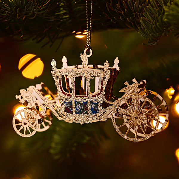 Handcrafted Gold State Coach Christmas Tree Ornament, featuring intricate 24-carat gold details. A stunning royal carriage replica by The London Christmas Company, perfect for adding British elegance to your festive decor. Seen here hanging in a Christmas tree.