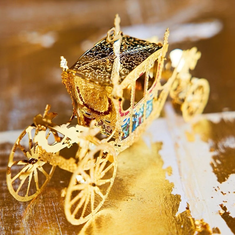 Handcrafted Gold State Coach Christmas Tree Ornament, featuring intricate 24-carat gold details. A stunning royal carriage replica by The London Christmas Company, perfect for adding British elegance to your festive decor. Seen here on a golden table.