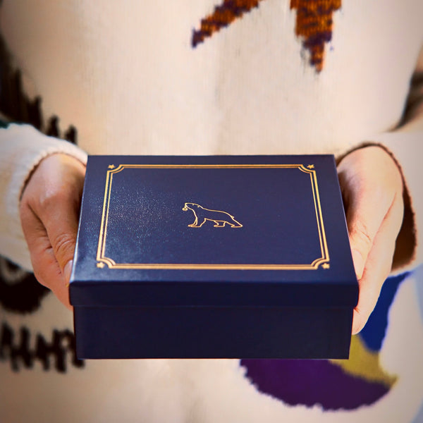 Woman's hands holding luxury blue gift box with gold details and The London Christmas Company logo.