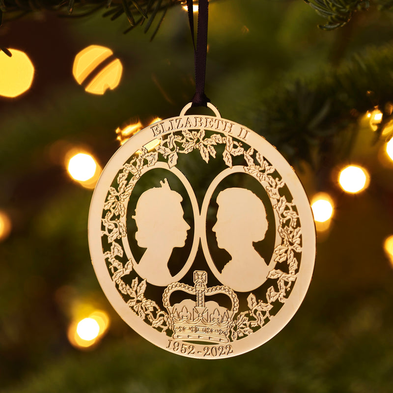 Handcrafted Gold Plated Queen Elizabeth II Commemorative Christmas Ornament, pictured hanging in a Christmas tree, it features intricate detailing, from The London Christmas Company. Celebrate British royal legacy with this elegant holiday keepsake