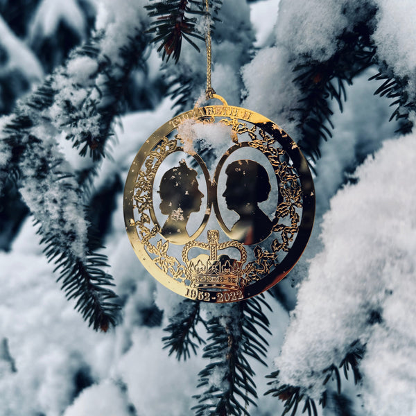 Handcrafted Gold Plated Queen Elizabeth II Commemorative Christmas Ornament, pictured hanging in a snowy tree, it features intricate detailing, from The London Christmas Company. Celebrate British royal legacy with this elegant holiday keepsake