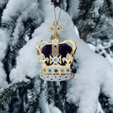 Handcrafted St Edward’s Crown Christmas Tree Ornament, hanging in a snowy tree - intricate 24-carat gold detailing and vibrant jewel embellishments. A royal symbol of British heritage by The London Christmas Company.