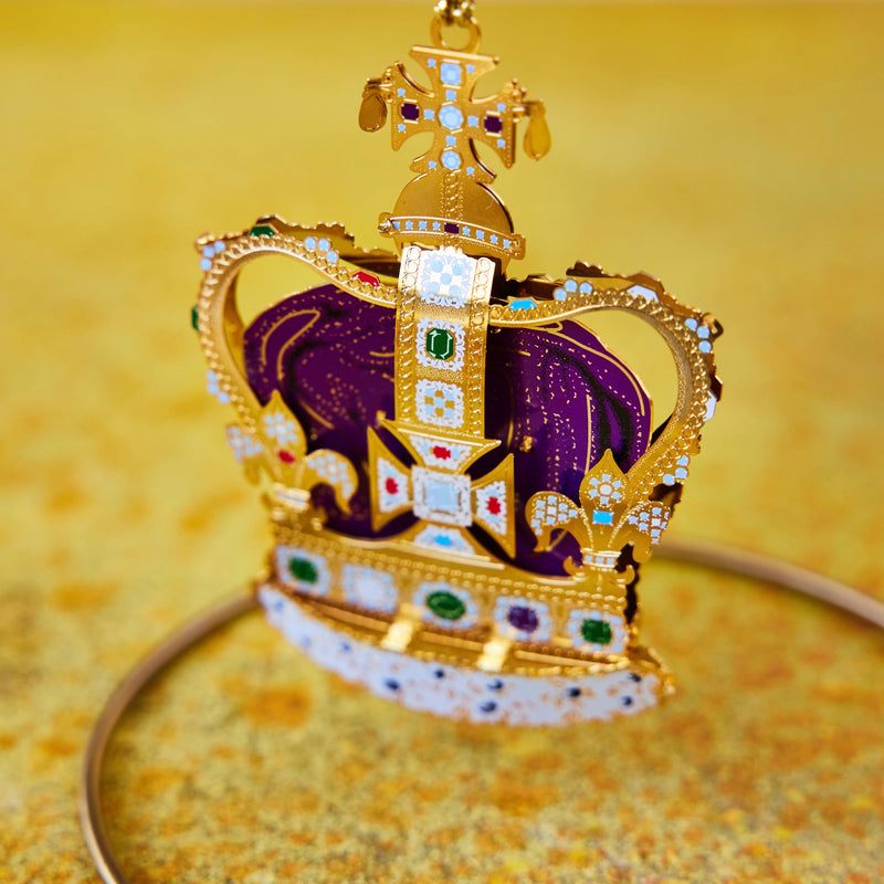 Handcrafted St Edward’s Crown Christmas Tree Ornament, hanging on a ornament stand, featuring intricate 24-carat gold detailing and vibrant jewel embellishments. A royal symbol of British heritage by The London Christmas Company.